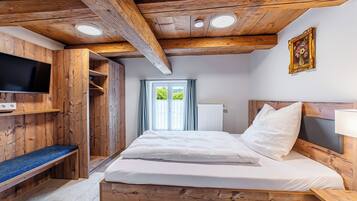 Ein Zimmer aus Holz mit einem Bett, einer Bank, einem Fernseher und einem Fenster mit Vorhängen.