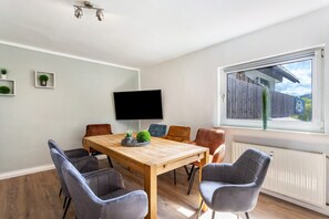 Un coin repas avec une table en bois, six chaises, un téléviseur à écran plat et une fenêtre donnant sur une clôture en bois.