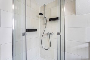 Une douche fermée par des parois en verre, dotée d’un pommeau de douche à main et d’un robinet mural.