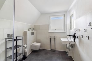 Een badkamer met een toilet, een wastafel, een spiegel, een plank met toiletartikelen en een klein raam.