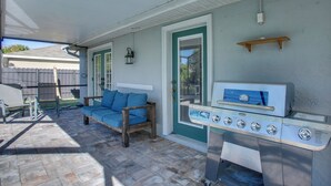 A covered patio with a grill, a blue cushioned bench, and a door with a green frame. - 3 Mi to Sun Splash Waterpark! Family Haven w/ Pool (Cape Coral)
