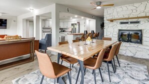 A modern kitchen with a stone wall, a dining area with a wooden table and chairs, and a built-in fireplace. - Patio + Golf Course Views: Monkey Island Escape! (Afton)