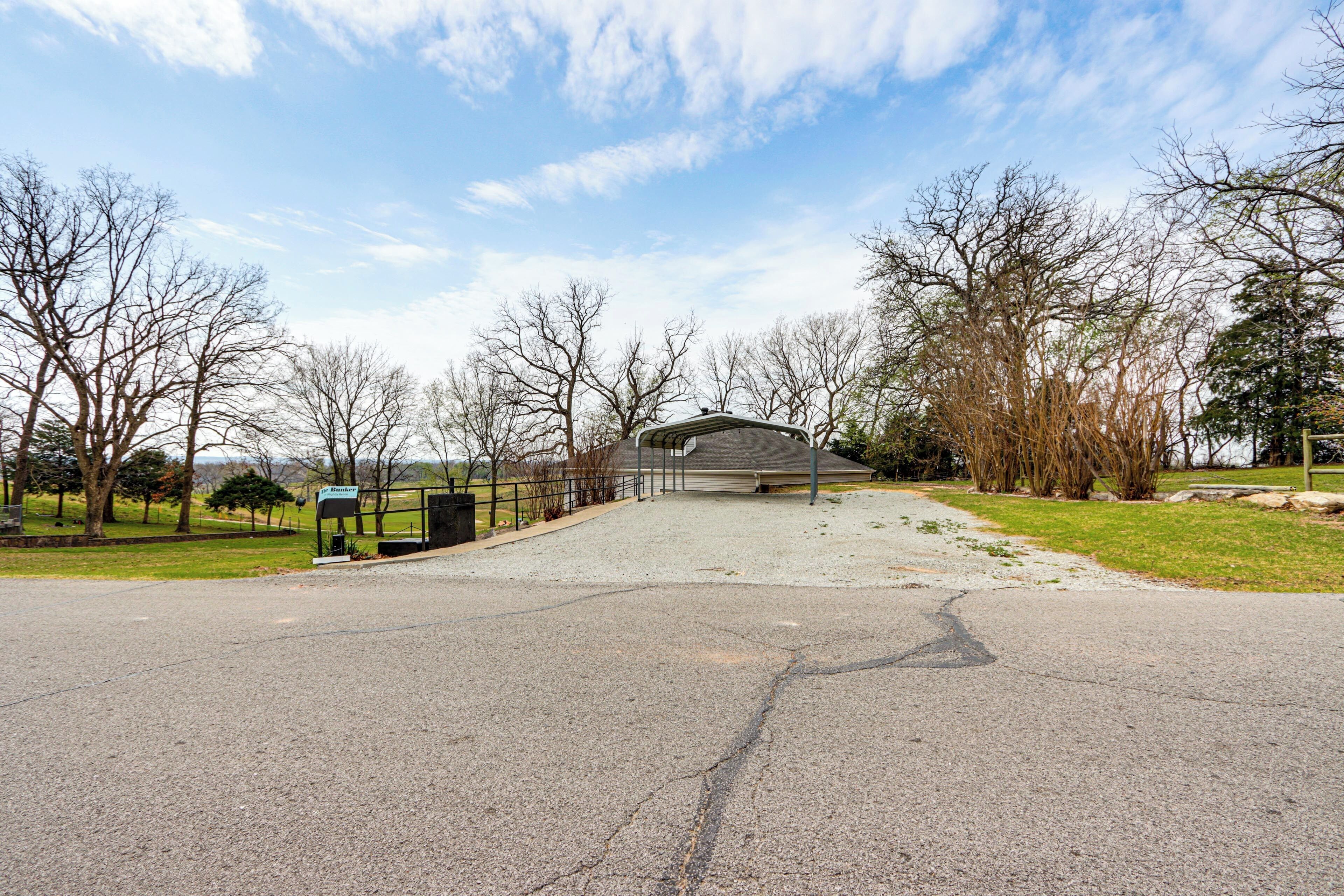 A paved driveway leading to a building with a covered entrance, surrounded by trees and a grassy area.