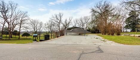 A paved driveway leading to a building with a covered entrance, surrounded by trees and a grassy area.