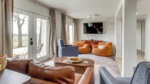 A spacious living room with a large TV, leather sofas, and a view through the glass doors. - Patio + Golf Course Views: Monkey Island Escape! (Afton)