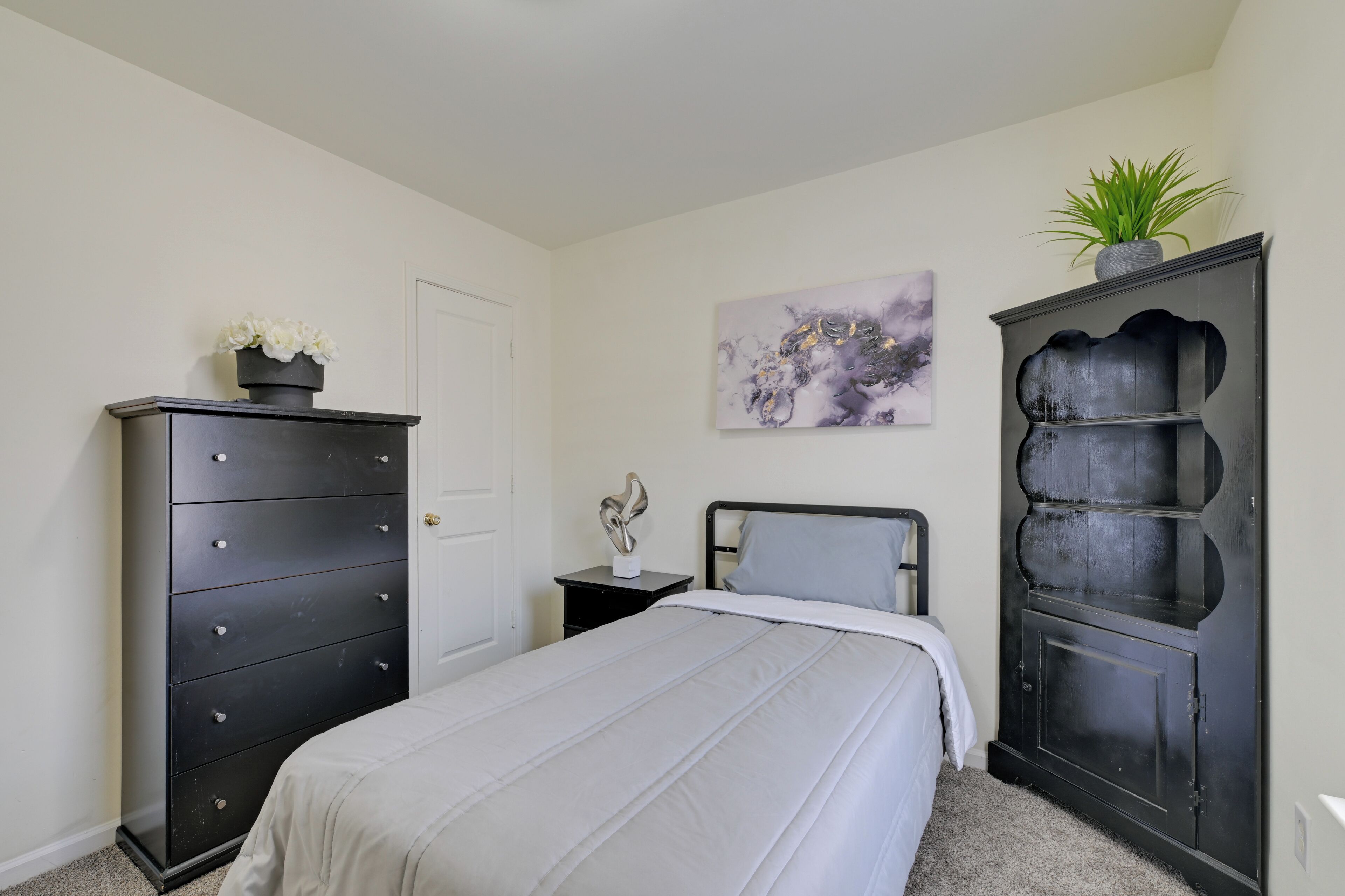Quarto com cama, cômoda, mesa de cabeceira, prateleira na parede e um quadro.