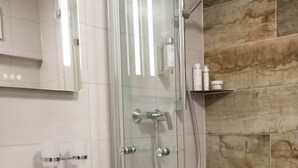 Une salle de bain moderne avec une douche à parois de verre, un lavabo blanc et un mur en pierre de couleur beige.