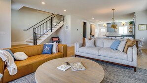 A living room with a staircase, two sofas, a coffee table, and a kitchen in the background. - 'bearly Behaven' Near Bear Lake & Marina! (Garden City)