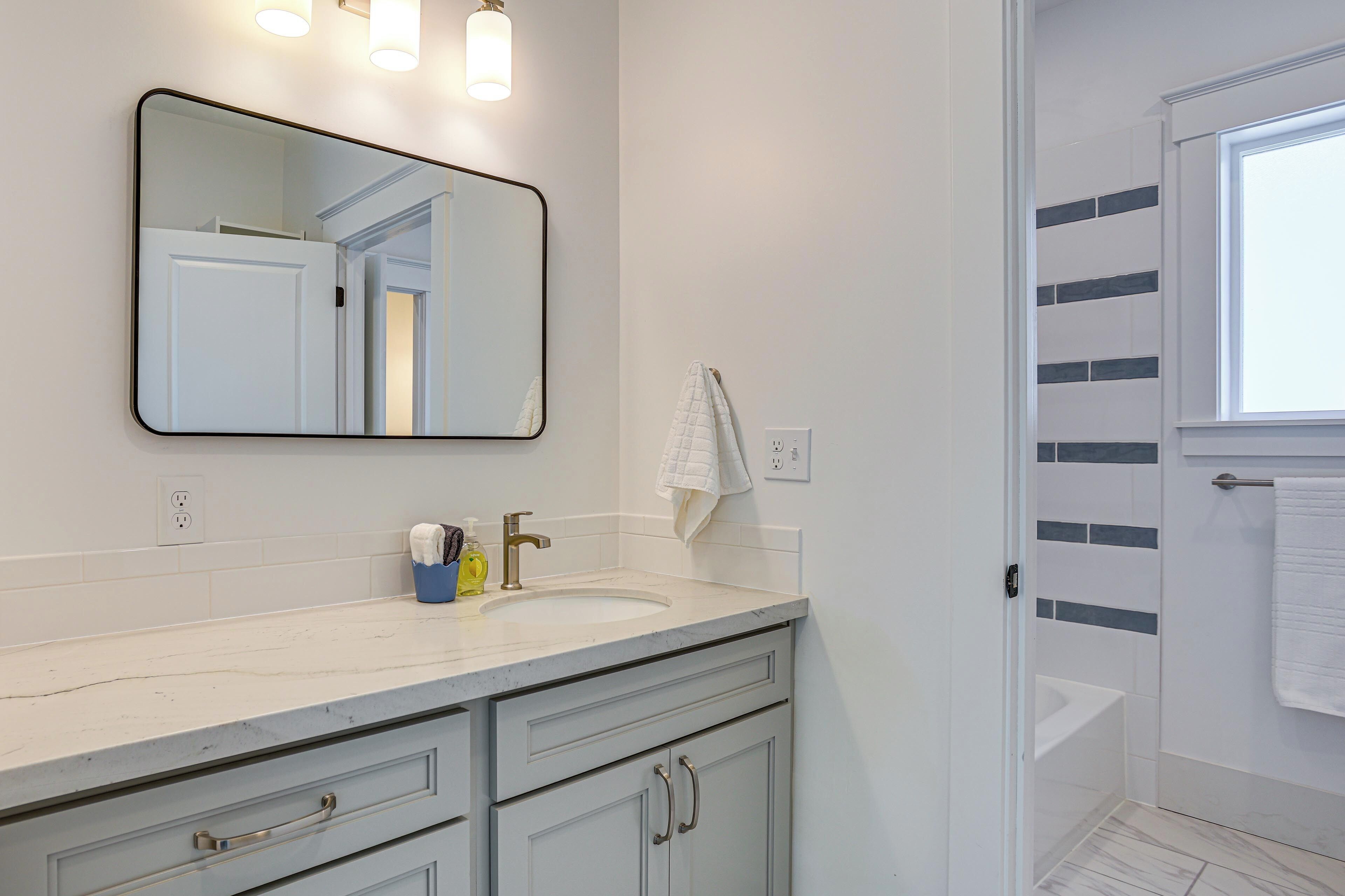 Un bagno con un lavandino bianco, uno specchio e un portascopino.