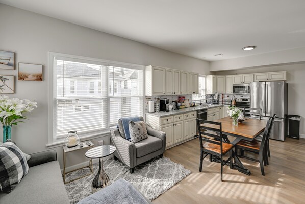 A modern kitchen with white cabinets, a dining table with chairs, a sofa with a patterned throw, and a window with blinds. - 1 Mi to Beach! Family-friendy Atlantic City Escape (Atlantic City)