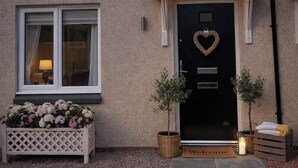 Ein Haus mit einer schwarzen Haustür, einer herzförmigen Dekoration, zwei Blumentöpfen, einer Fußmatte und Solaranlagen auf dem Dach.