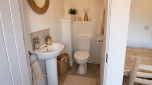 Ein kleines Badezimmer mit Waschbecken, Toilette und Spiegel, einer Pendelleuchte und einer kleinen Ablagefläche mit Dekoration.