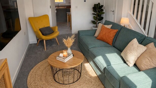 Ein Wohnzimmer mit einem grünen Sofa, einem gelben Sessel, einem runden Couchtisch und einer Pendelleuchte.