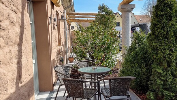 A patio with a round table and chairs, a pergola, and a stone pillar.