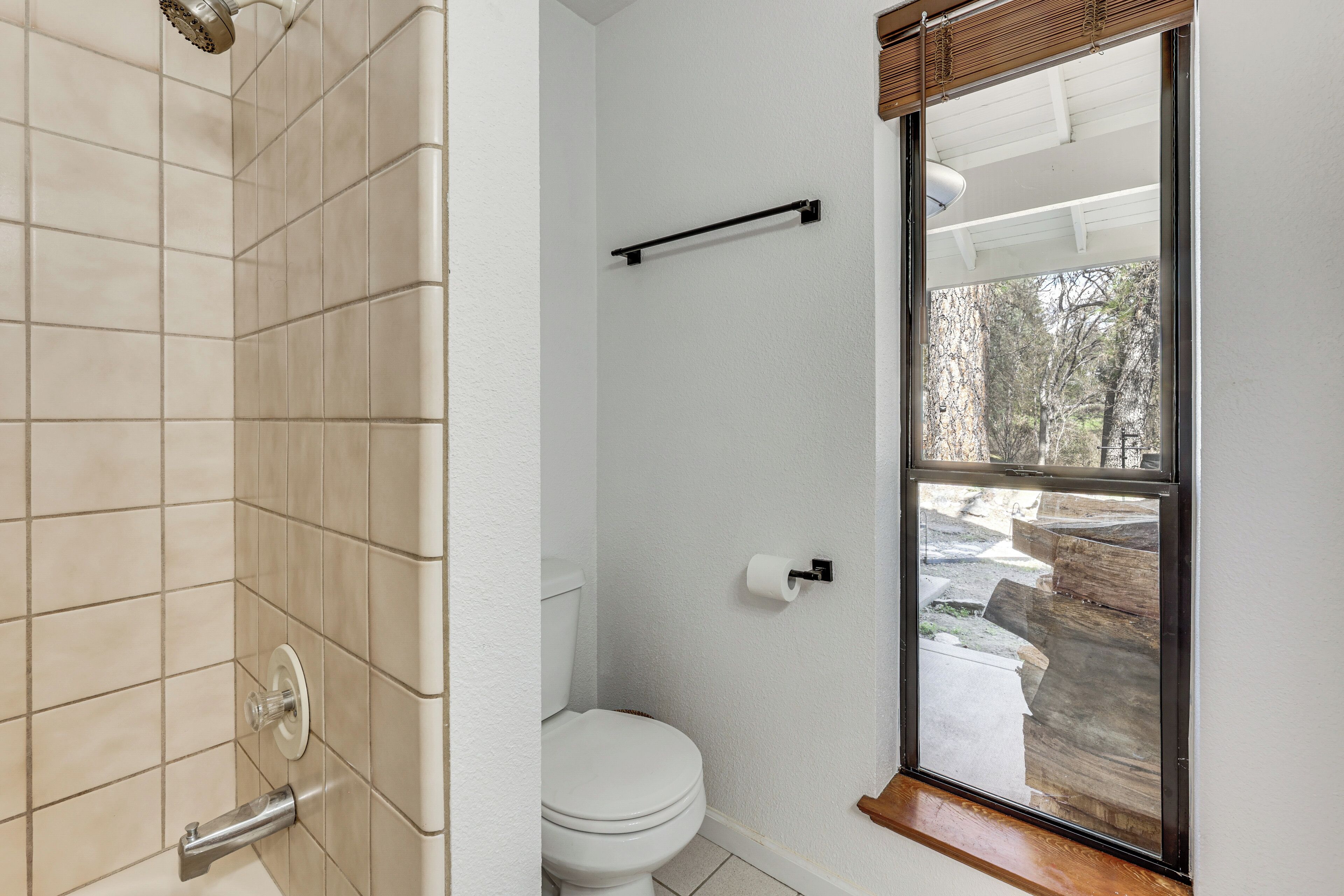 Een badkamer met douche, toilet en raam met uitzicht op bomen.