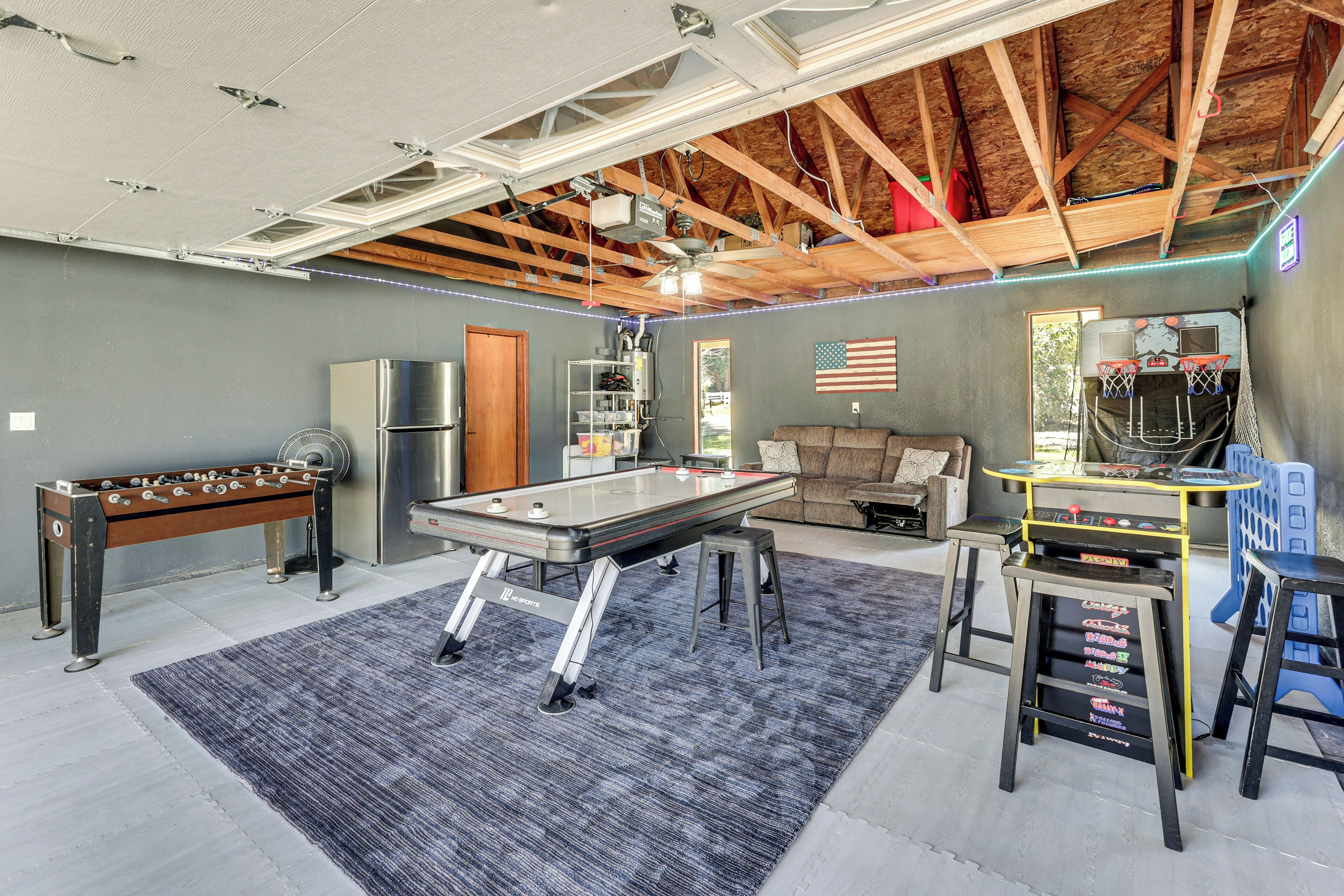 A spacious room with a foosball table, a pool table, a ceiling fan, and a basketball hoop.