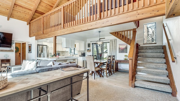 Una cocina amplia con techo alto, un comedor con sillas de madera y una escalera que sube a un nivel superior.