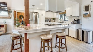Una cocina moderna con armarios blancos, un refrigerador de acero inoxidable, una isla grande con taburetes y una máquina de café.