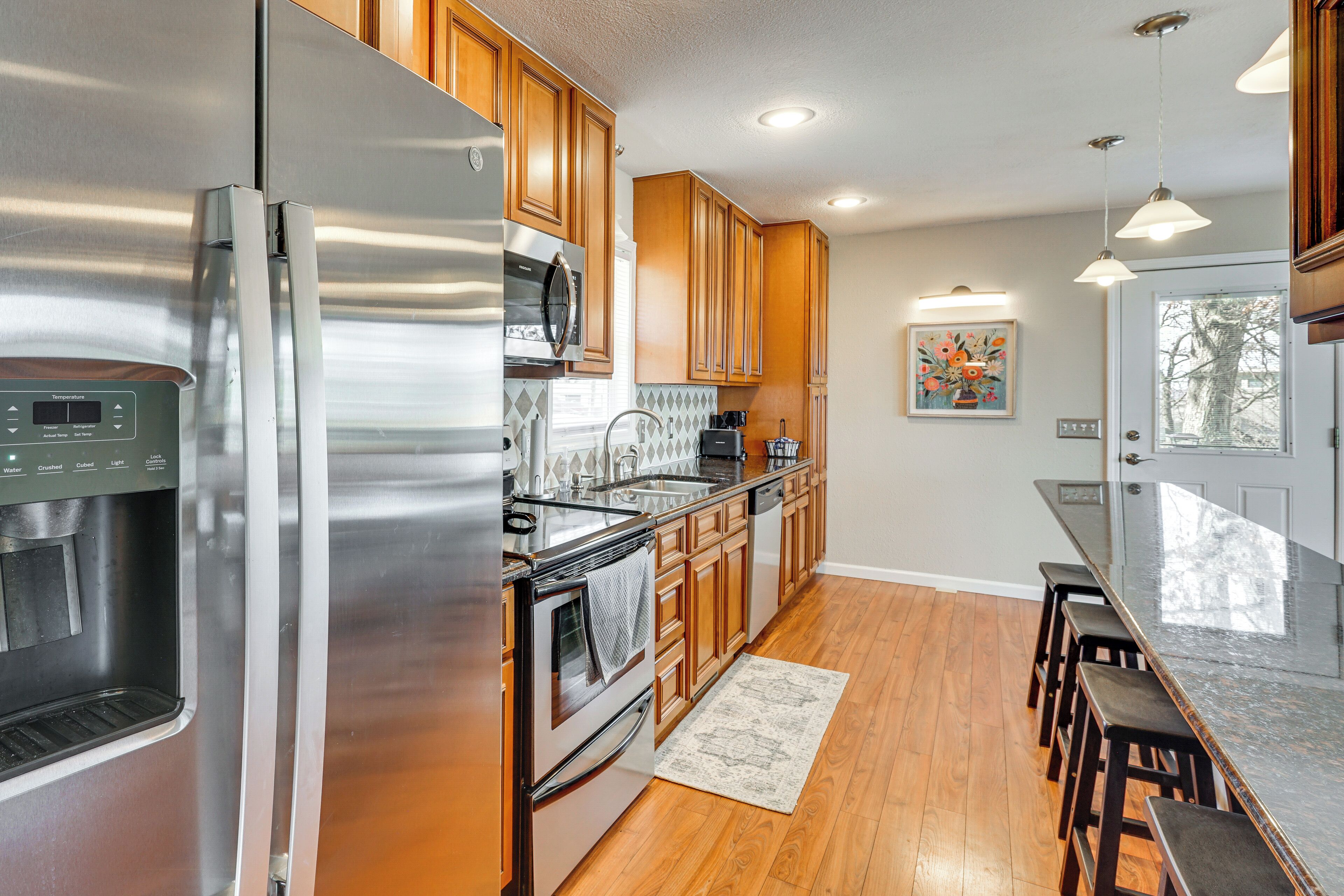 A modern kitchen with stainless steel appliances, wooden cabinets, and a bar area.