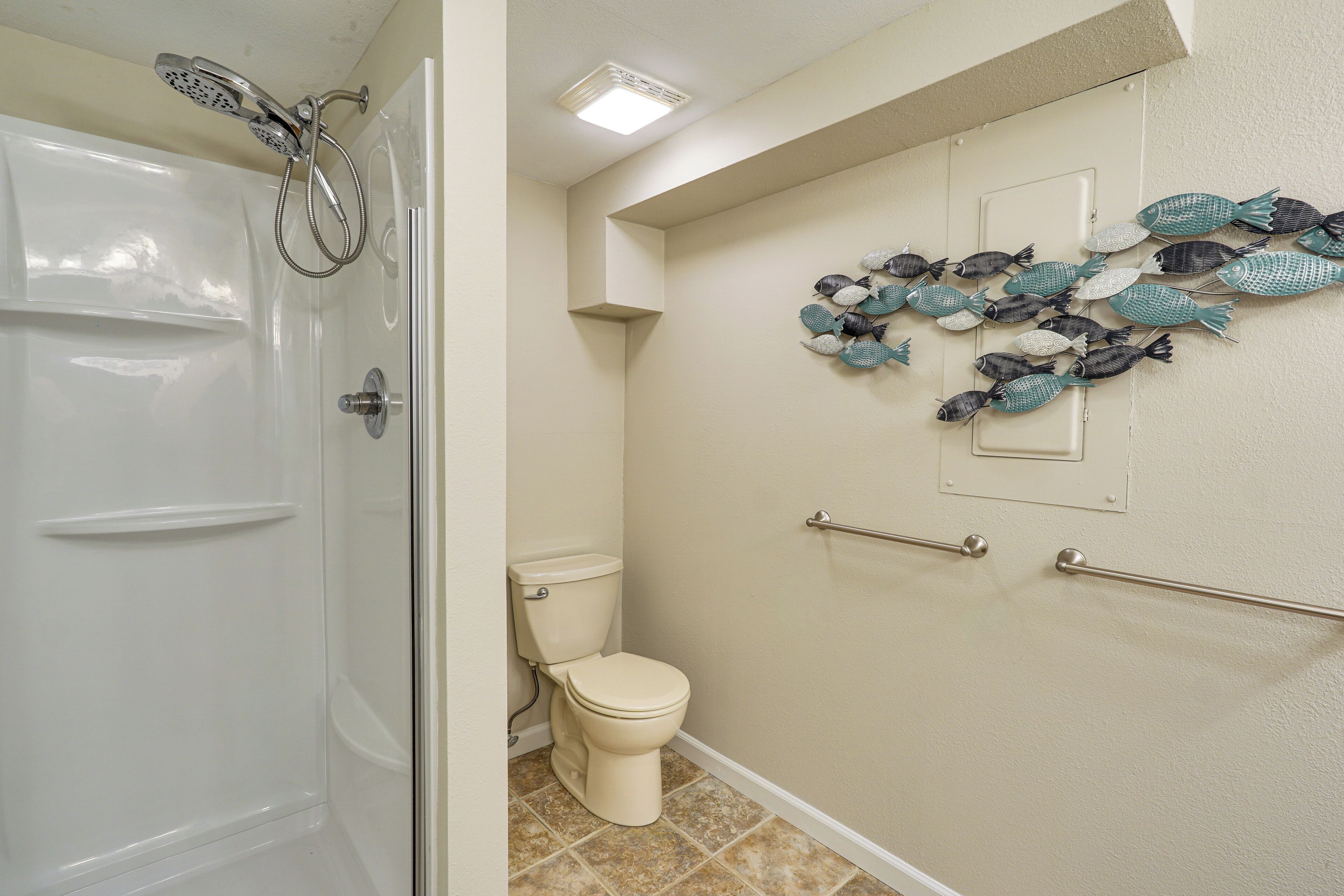 A bathroom with a shower, toilet, and decorative fish wall art.