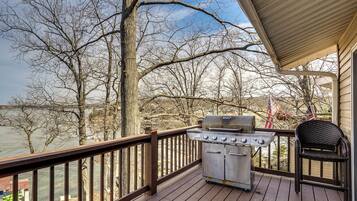 A deck with a grill, a chair, and a view of a lake.