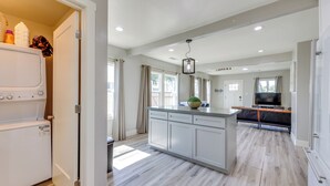 A modern kitchen with a central island, a built-in washer-dryer unit, and a dining area with a TV. - < 1 Mi to Main St Hanford! Home w/ Outdoor Space (Hanford)
