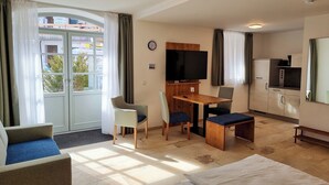 Une chambre d’hôtel comprenant un lit, un bureau, deux chaises, une télévision, une horloge et une kitchenette.