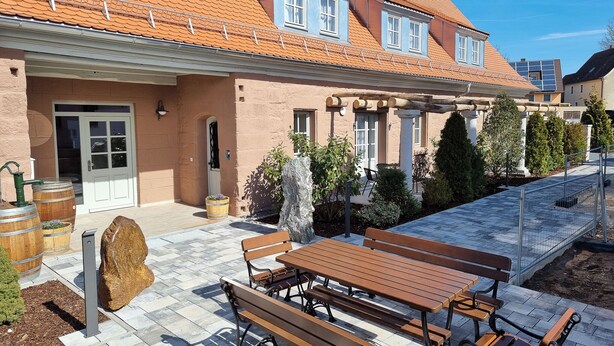 Une maison avec un toit en tuiles, un patio couvert avec une table et des bancs, et une porte avec une fenêtre.
