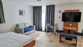 Quarto de hotel com cama, sofá, televisão, escrivaninha e cadeira.