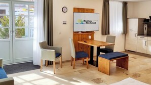 Une pièce comprenant une table à manger, des chaises, une horloge, un panneau et un coin cuisine.