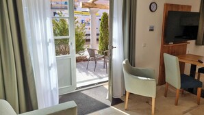 Une pièce dotée d’une porte-fenêtre coulissante donnant sur un espace extérieur, d’un bureau en bois avec une chaise, d’un téléviseur fixé au mur et d’une horloge.