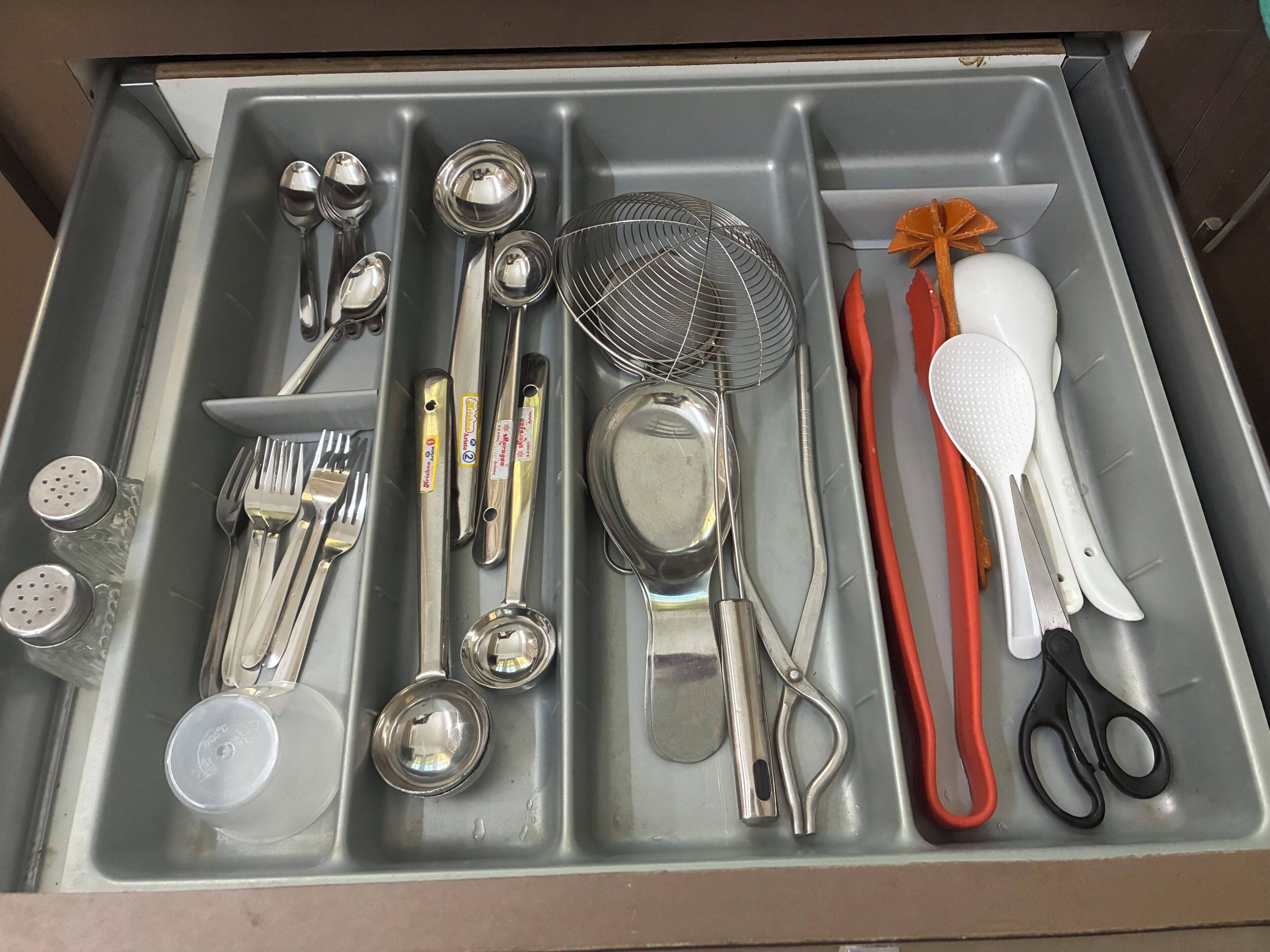 A drawer with various utensils and kitchenware, including forks, spoons, a whisk, and a pair of scissors.