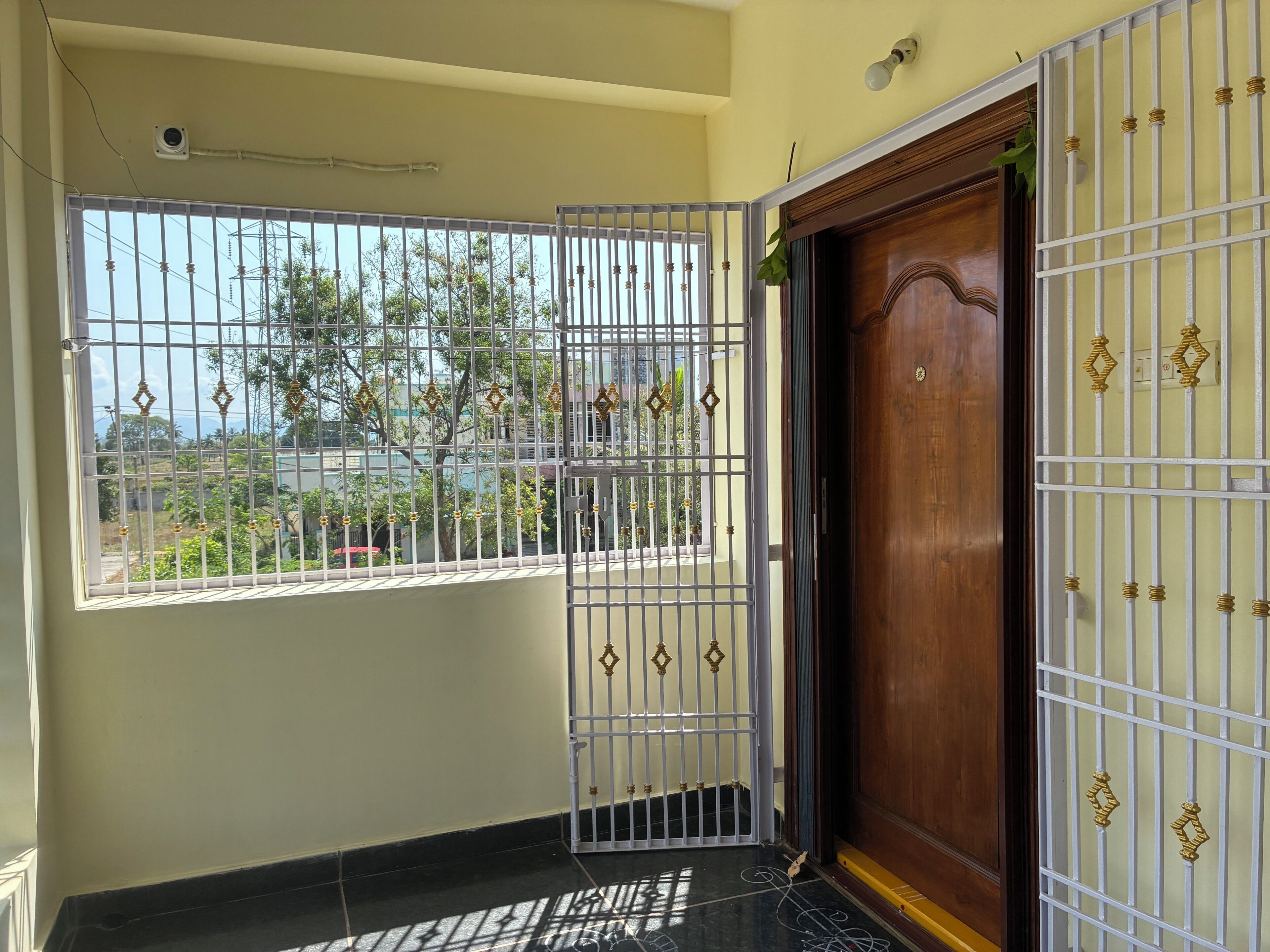 Una habitación con ventana protegida por barrotes, una puerta de madera y una cámara de seguridad instalada en el techo.
