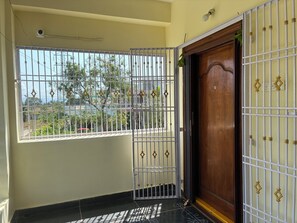 Ein Zimmer mit vergittertem Fenster, einer Holztür und einer unter der Decke befestigten Überwachungskamera.
