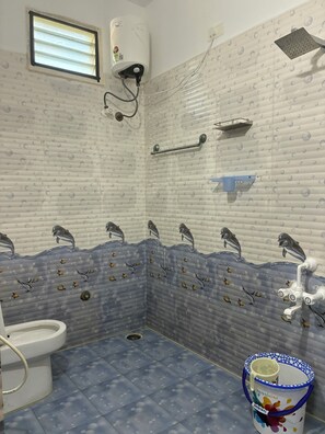 Un bagno con decorazioni a tema delfini sui piastrelle, un water, una doccia e un secchio con manico.