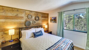 A bedroom with a wooden headboard, a bed with white bedding, two bedside tables with lamps, and a window with a view of trees. - 1 Mi to Woodland Lake! Cabin w/ Dog-friendly Yard (Pinetop)