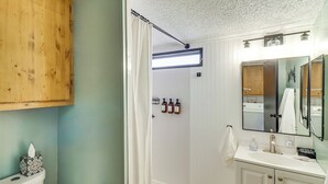 A bathroom with a toilet, a shower curtain, a sink with a mirror, and toiletries on the wall. - 1 Mi to Woodland Lake! Cabin w/ Dog-friendly Yard (Pinetop)