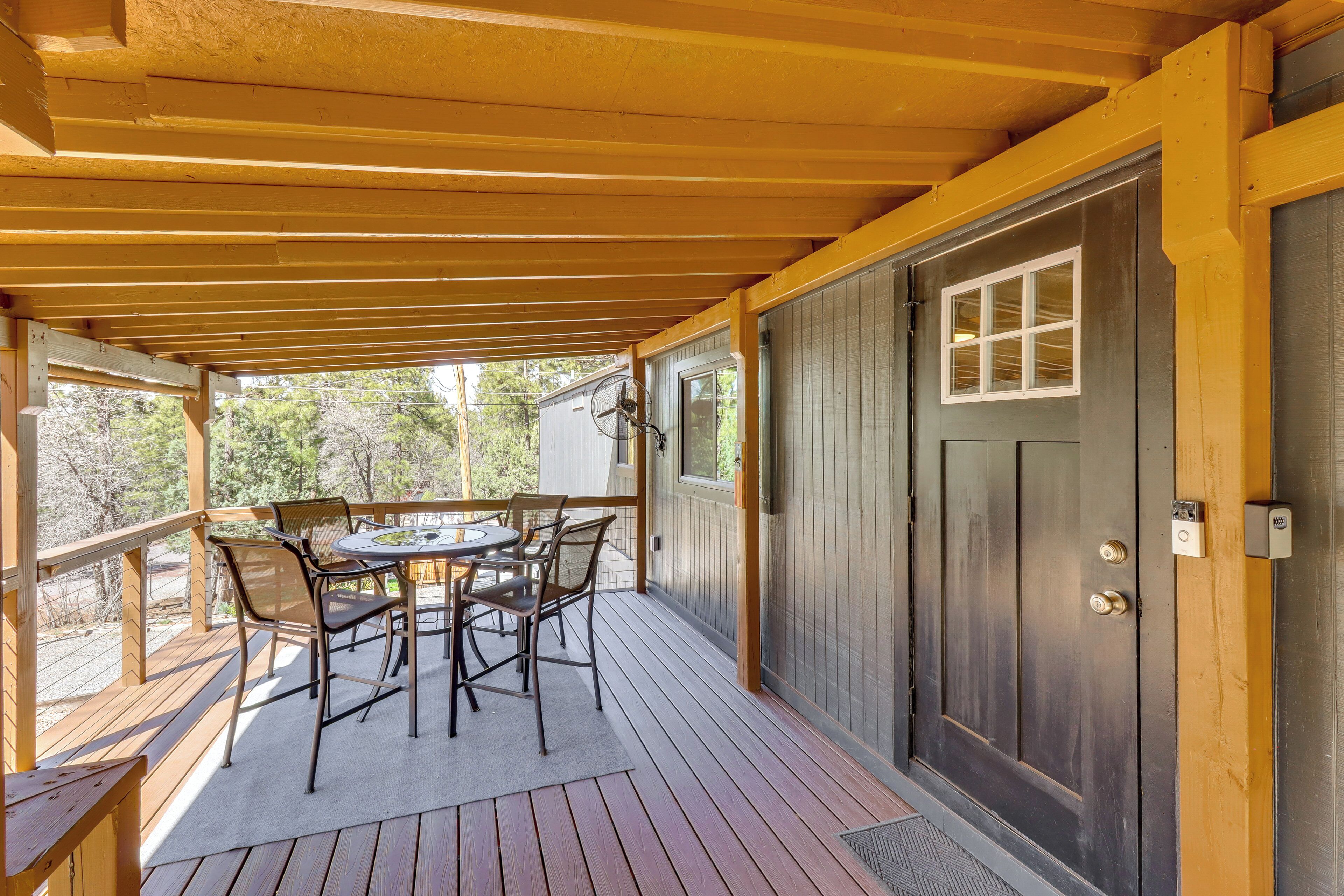 A covered outdoor patio with a table and chairs, a door with a window, and a wooden deck.