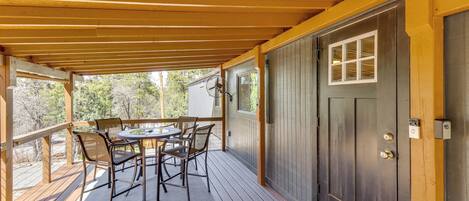 A covered outdoor patio with a table and chairs, a door with a window, and a wooden deck.