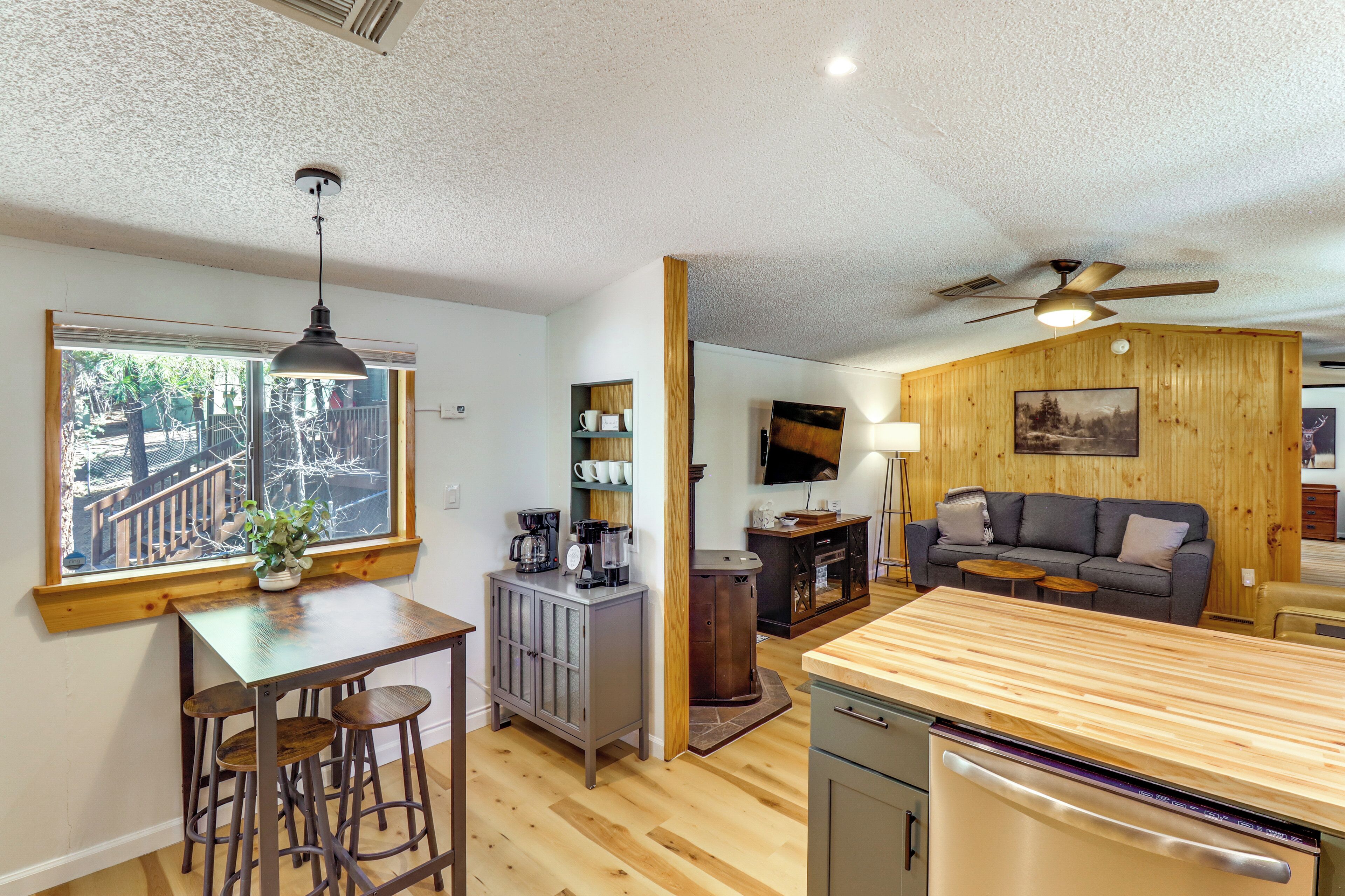 A kitchen with a wooden countertop, a dining area with stools, a coffee station, and a living area with a sofa and a TV.