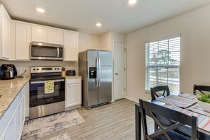 A kitchen with white cabinets, stainless steel appliances, a dining table with a plant, and a window with blinds. - Sleek + Convenient Palm Bay Stay: Bring Your Pet! (Palm Bay)