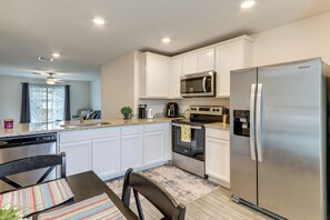 A modern kitchen with white cabinets, stainless steel appliances, and a dining area with a table and chairs. - Sleek + Convenient Palm Bay Stay: Bring Your Pet! (Palm Bay)