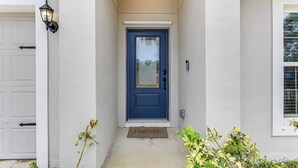 A blue door with a doormat, a white garage door, and a small plant beside the door. - Sleek + Convenient Palm Bay Stay: Bring Your Pet! (Palm Bay)