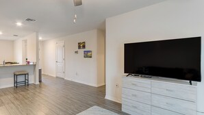 A modern living room with a flat-screen TV, a light-colored wooden cabinet, a small stool, and a rug. - Sleek + Convenient Palm Bay Stay: Bring Your Pet! (Palm Bay)