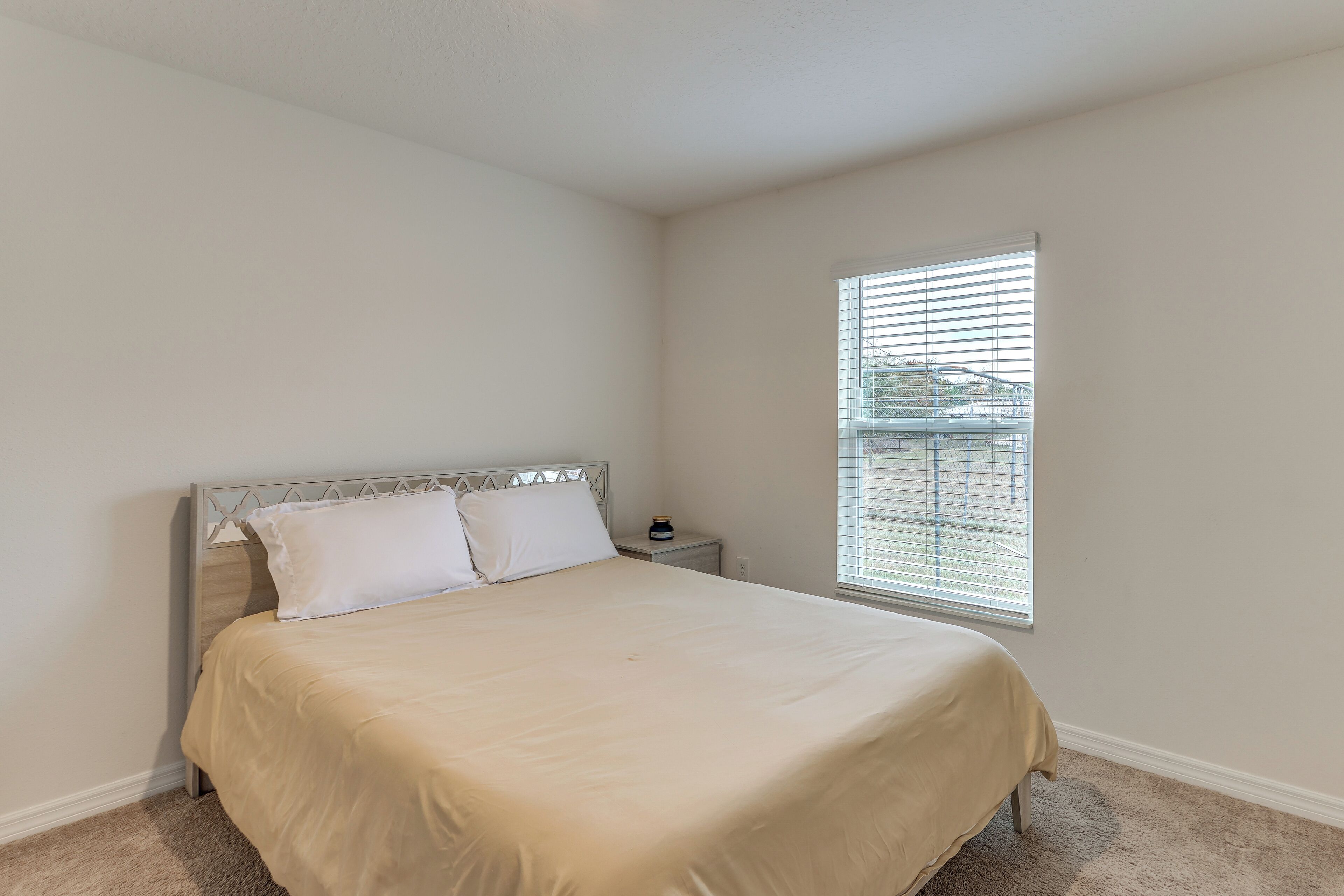 A bedroom with a bed, a nightstand, and a window with blinds.