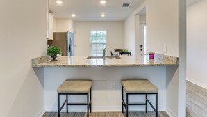 A kitchen with a granite countertop, two bar stools, a window, and a stainless steel refrigerator. - Sleek + Convenient Palm Bay Stay: Bring Your Pet! (Palm Bay)