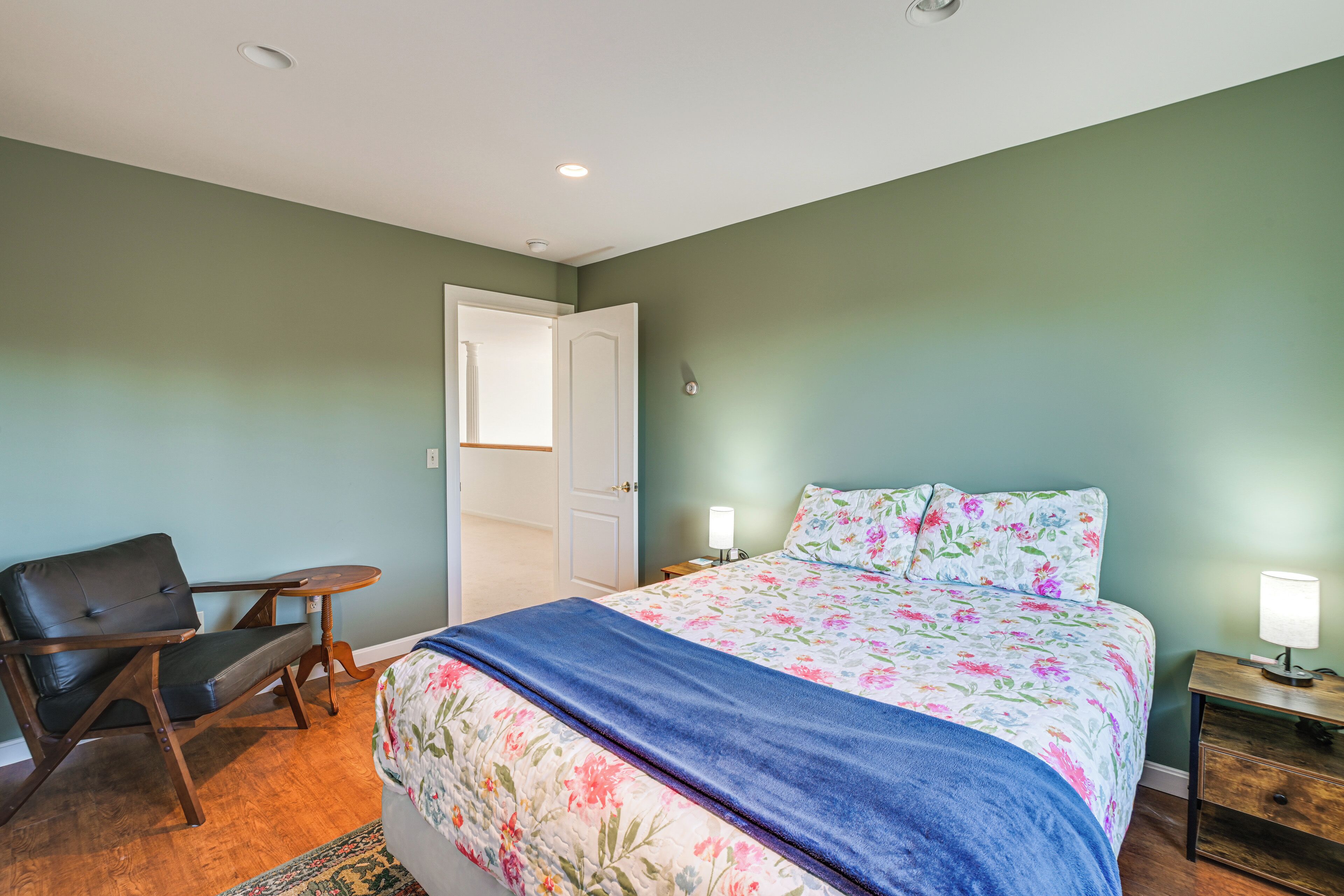 A bedroom with a bed, a chair, a nightstand, and a door.