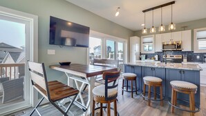 A modern kitchen with a large island, bar stools, and a dining area with chairs. - New Oak Island Home w/ Ocean Views! (Oak Island)