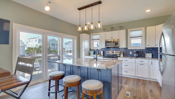 A kitchen with a large island, white cabinets, and a view to the outside. - New Oak Island Home w/ Ocean Views! (Oak Island)