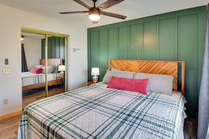 Un dormitorio con cama, ventilador de techo, mesita de noche con lámpara y espejo.